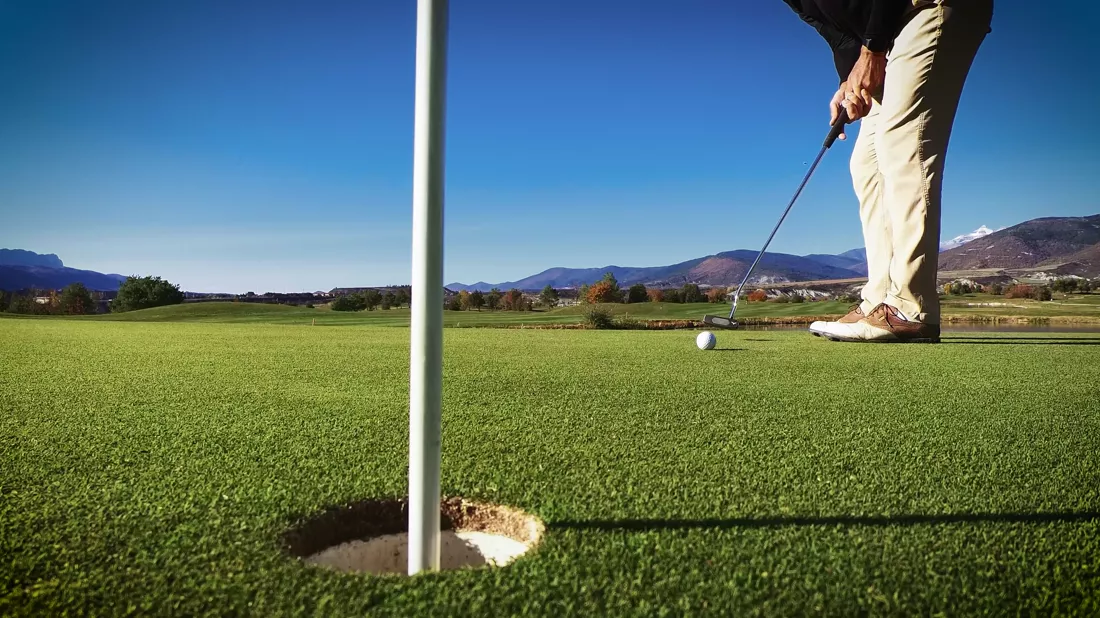 Golfer sinking a putt on a sunlit course
